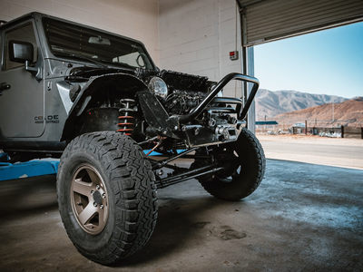 Jeep Wrangler front axle, track bar, and steering linkage being inspected on a shop lift near the Colorado foothills.