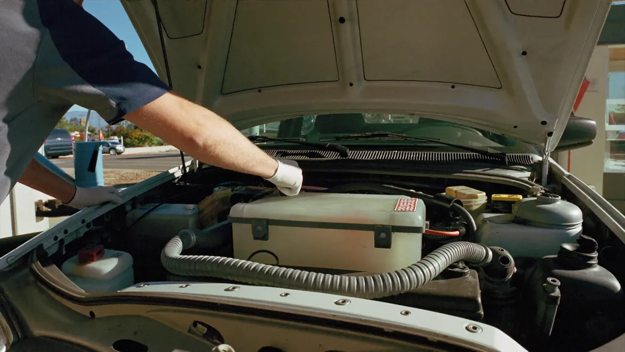 A mechanic examining the coolant reservoir under an open car hood.